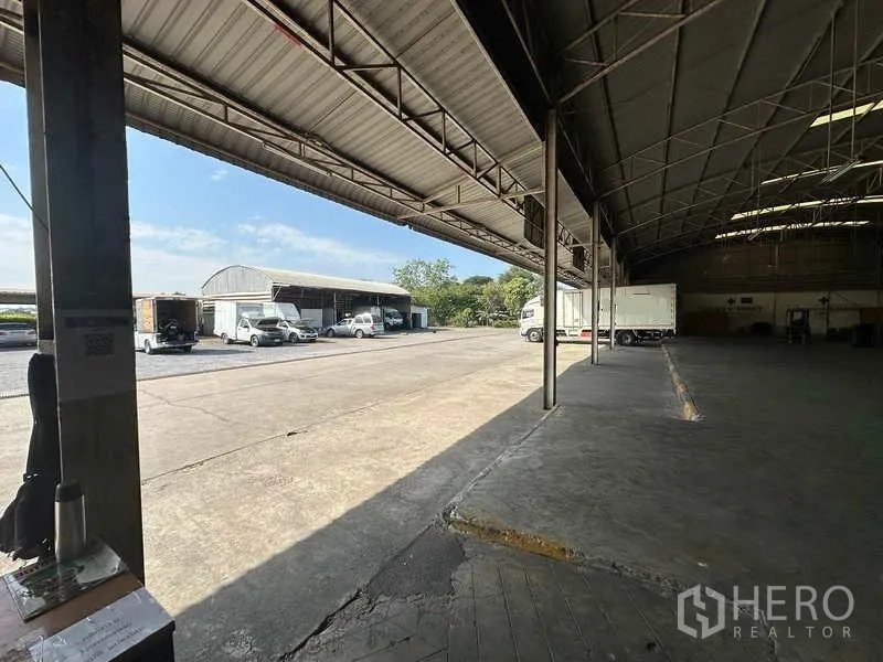 Warehouse for rent in Lam Luk Ka, Pathum Thani - View from loading dock toward yard with trucks and secondary shed.