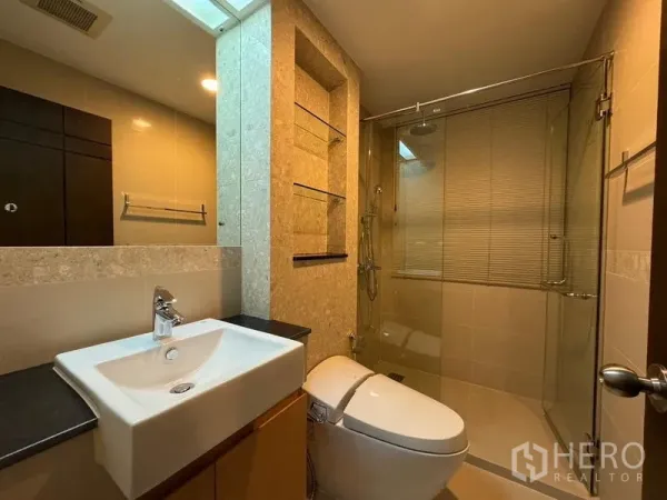 Condominium for rent in Pathum Wan, Bangkok - Modern bathroom with glass-enclosed shower, vanity sink, and wall niche shelves.