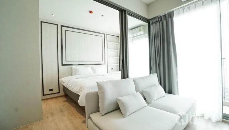 Condominium for sale in Khlong Toei, Bangkok - Lounge area facing a bedroom behind sliding doors, floor-to-ceiling curtains and private balcony.