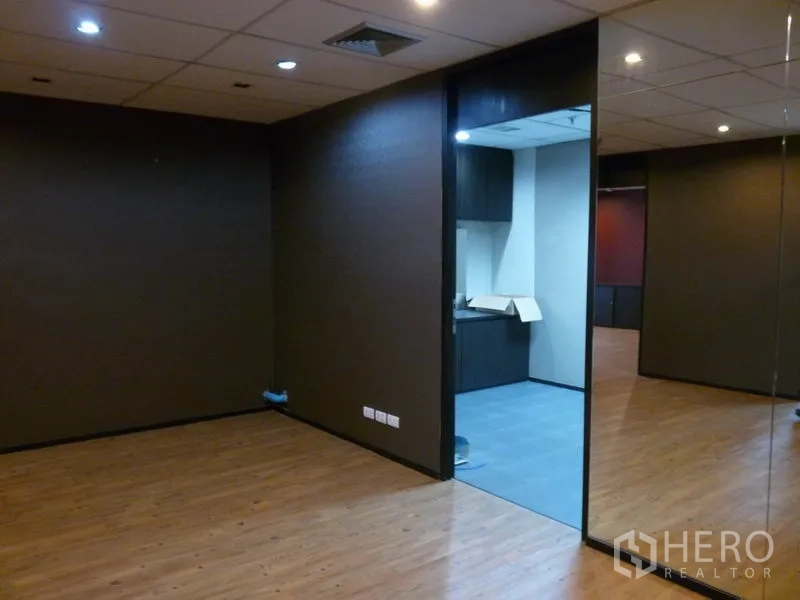 Office Space for rent in Watthana, Bangkok - Private office zone with dark walls and recessed lighting, opening to a pantry with grey tiles and cabinets.