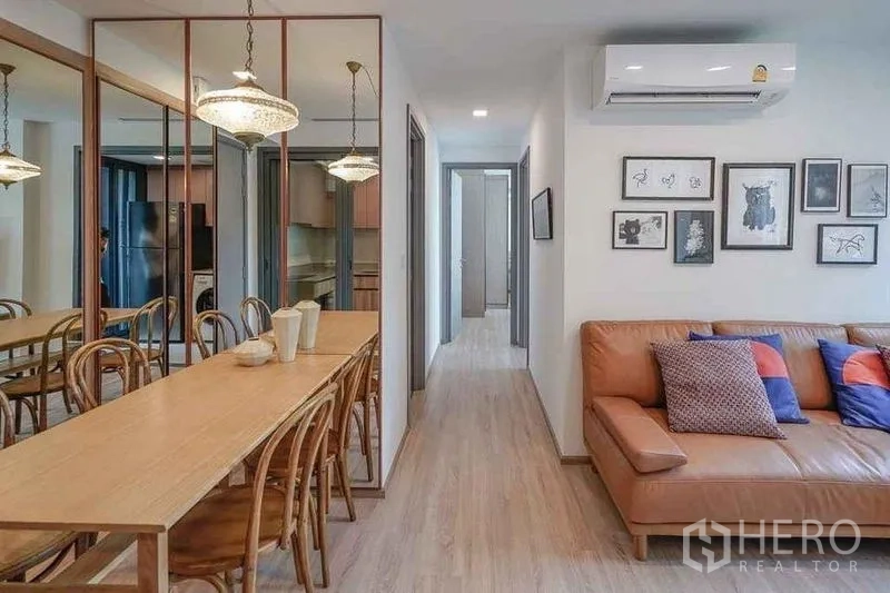 公寓 出租在Watthana, Bangkok - 餐厅设长木桌、镜面墙与吊灯，临近客厅。