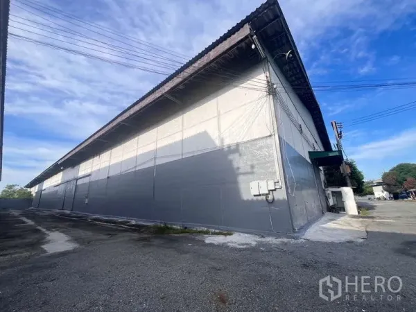 Factory for rent in Bang Pakong, Chachoengsao - Exterior of the warehouse building with gable roof, service cabling, and wide driveway for truck access.