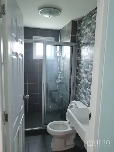 Townhouse for rent in Bang Kapi, Bangkok - Modern bathroom with glass-enclosed shower, grey tiles and white sanitary ware.