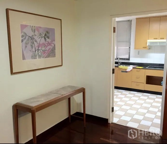 Condominium for rent in Watthana, Bangkok - Entry nook with wall art and console table opening to a separate kitchen with checkered flooring and light wood cabinets.
