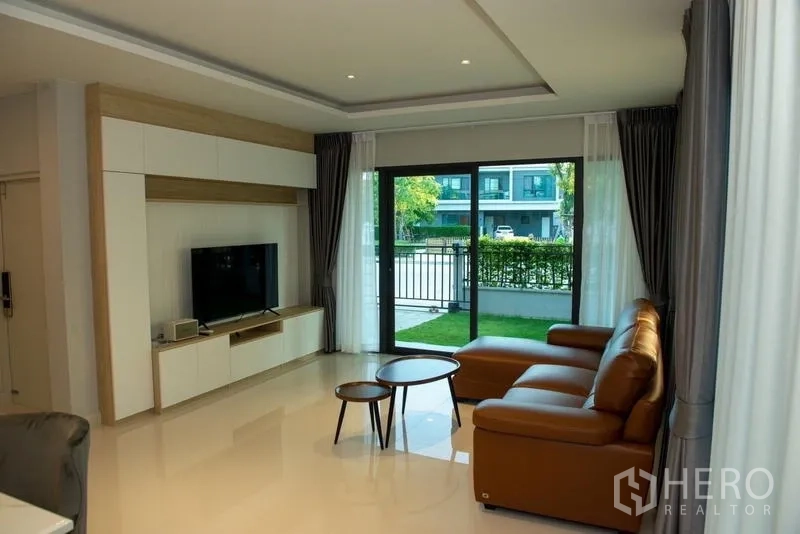 Detached House for rent in Bang Phli, Samut Prakan - Bright living room with TV wall, leather sofa and garden access.