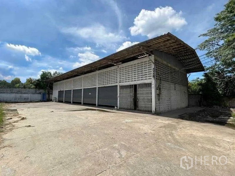 Warehouse for rent in Bang Na, Bangkok - Front exterior of the warehouse showing gated entrance, ventilated block walls, and expansive paved forecourt.