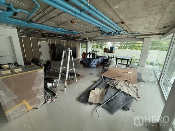 Retail Space for rent in Watthana, Bangkok - Unfinished retail interior with exposed ceiling pipes, floor-to-ceiling windows, and renovation materials.