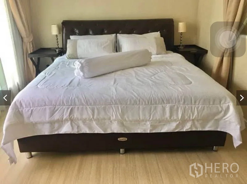 Townhouse for rent or sale in Suan Luang, Bangkok - Second bedroom with king-size bed, white bedding, bedside lamps, and natural light.