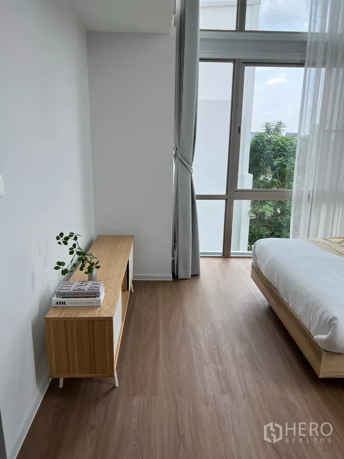 Detached House for rent in Saphan Sung, Bangkok - Sunlit bedroom corner with wood flooring, a low console and large windows with sheer curtains.