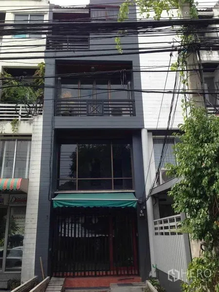 带办公室的家 出租或出售在Wang Thonglang, Bangkok - 整栋外观，深色立面与阳台的联排式居家办公楼，可见上方电线。