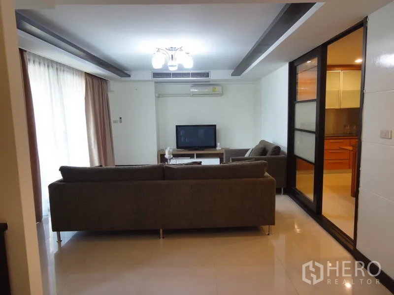 Condominium for rent in Watthana, Bangkok - Living area with sofa set facing TV and glass partition to the kitchen.