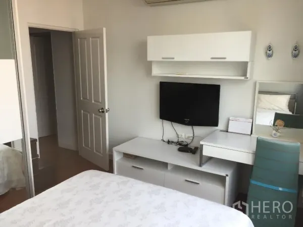 Condominium for rent or sale in Khlong Toei, Bangkok - Bright bedroom with white built-in furniture, wall-mounted TV, desk, and sliding wardrobe.