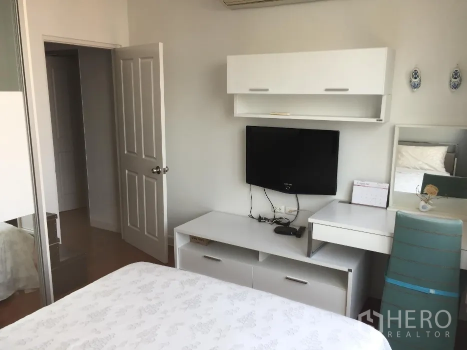 Condominium for rent or sale in Khlong Toei, Bangkok - Bright bedroom with white built-in furniture, wall-mounted TV, desk, and sliding wardrobe.