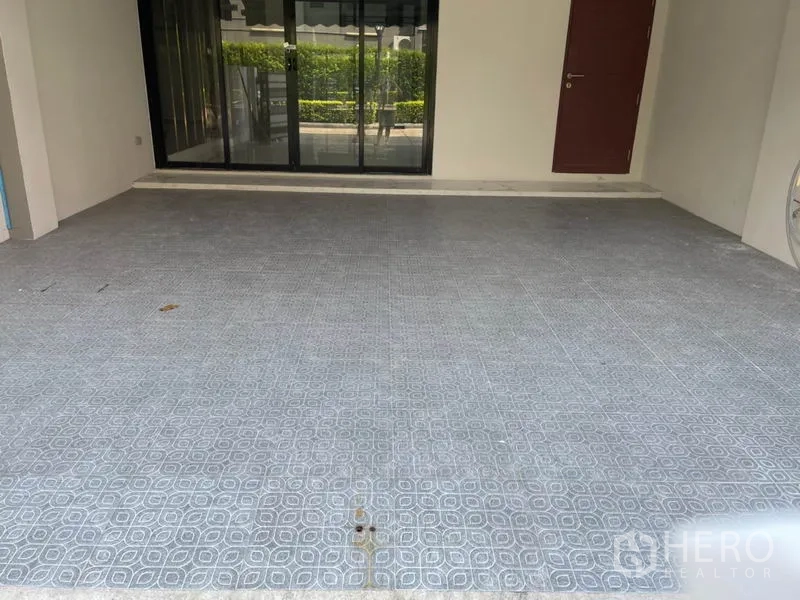 Townhouse for rent or sale in Yan Nawa, Bangkok - Covered carport with tiled floor facing glass sliding doors and trimmed greenery.