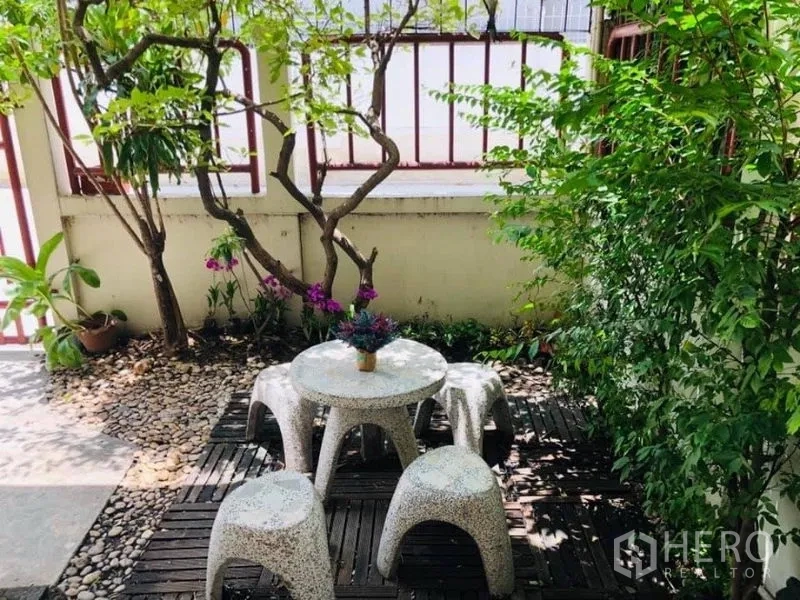 Detached House for rent in Watthana, Bangkok - Shaded patio corner with round stone table and stools amid greenery.