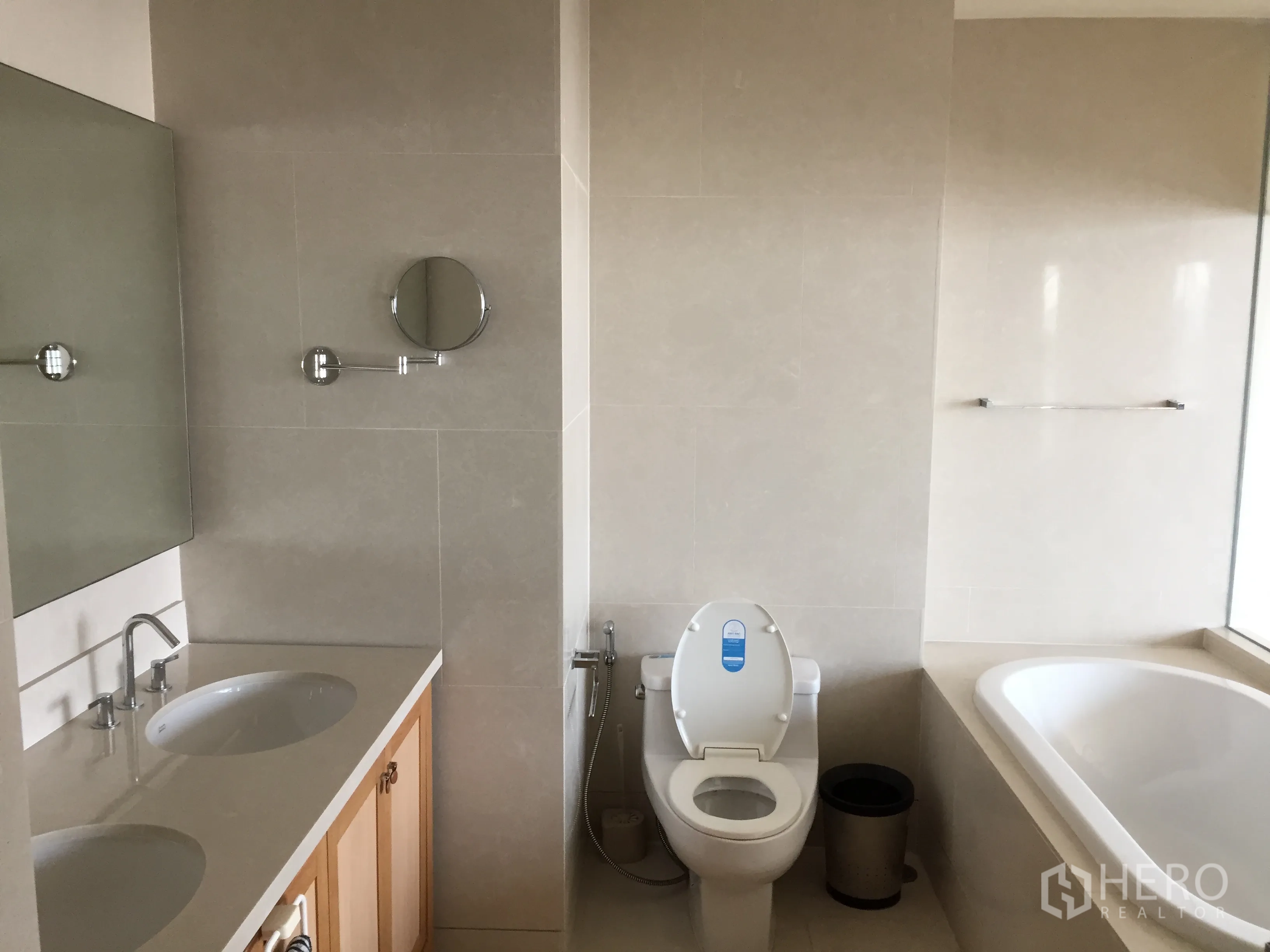 Condominium for rent or sale in Khlong Toei, Bangkok - Spacious bathroom with double-sink vanity, toilet and bathtub beside a window.