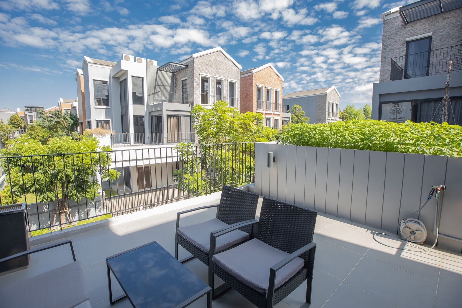 Detached House for rent in Lat Phrao, Bangkok - Balcony seating area with views of modern neighboring houses and lush greenery under blue sky.