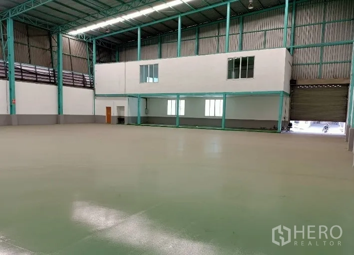 Factory for rent in Samut Prakan - Spacious factory hall with high steel truss roof, mezzanine office and a large roller shutter door.