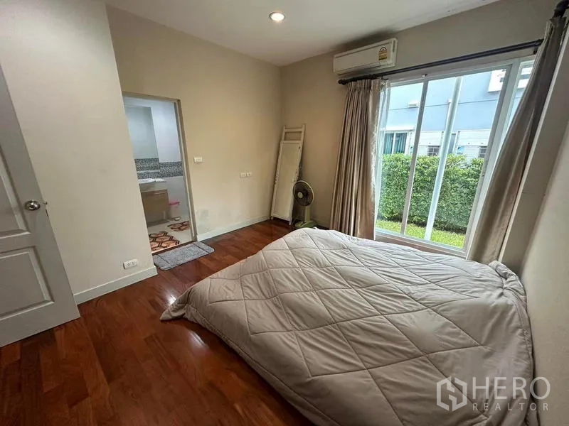 独立式住宅 出售在Saphan Sung, Bangkok - 卧室配木地板与落地窗，面向花园，并有套内浴室入口。