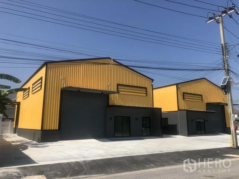 Factory for rent in Bang Yai, Nonthaburi - New twin yellow steel-clad factory buildings with a wide concrete driveway and loading area.