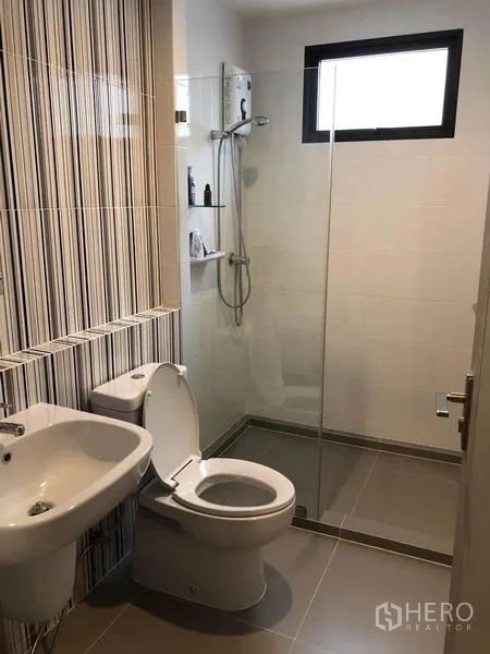 Townhouse for rent in Lat Phrao, Bangkok - Bright bathroom featuring a glass-enclosed shower, striped accent wall, sink and toilet.