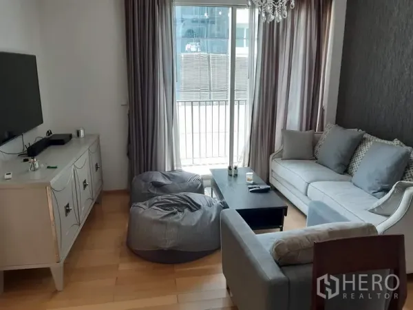 Condominium for rent in Khlong Toei, Bangkok - Bright living room with sofa set, TV console, wood floors and sliding doors to the balcony.