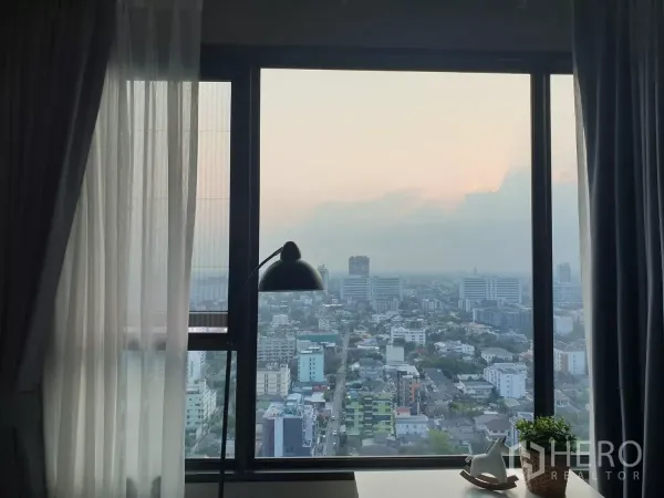 Condominium for rent in Chatuchak, Bangkok - High-floor window view over Chatuchak at sunset with curtains and desk lamp.