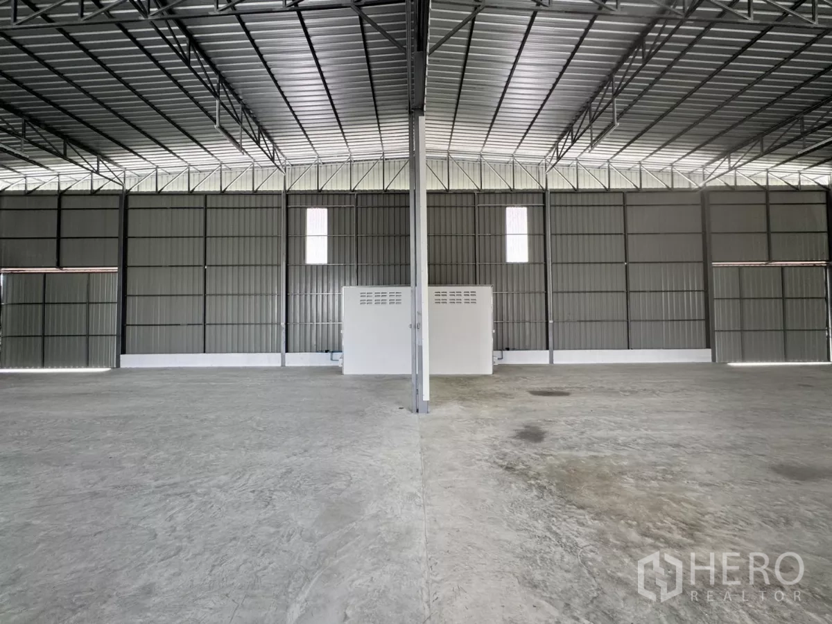 Warehouse for rent in Lam Luk Ka, Pathum Thani - Symmetrical interior view with a central column, small service room and expansive concrete floor.