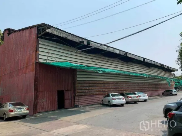 Warehouse for rent in Bang Kho Laem, Bangkok - Street view of a large corrugated‑metal warehouse with front parking and wide driveway.