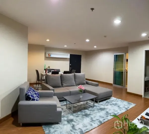 公寓 出租 - 宽敞客厅，灰色转角沙发、工作区与暖色灯光。