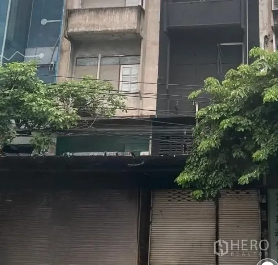 店屋 出租在Watthana, Bangkok - 通罗临街商铺外立面，可见卷帘门与路边绿树。