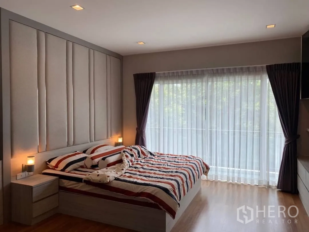 Detached House for rent or sale in Prawet, Bangkok - Master bedroom with padded headboard, floor-to-ceiling windows and sheer curtains.