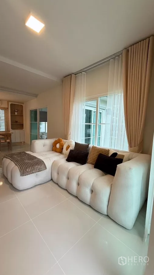 Detached House for rent in Bang Phli, Samut Prakan - Spacious living area with a large tufted sectional sofa and floor-to-ceiling curtains.