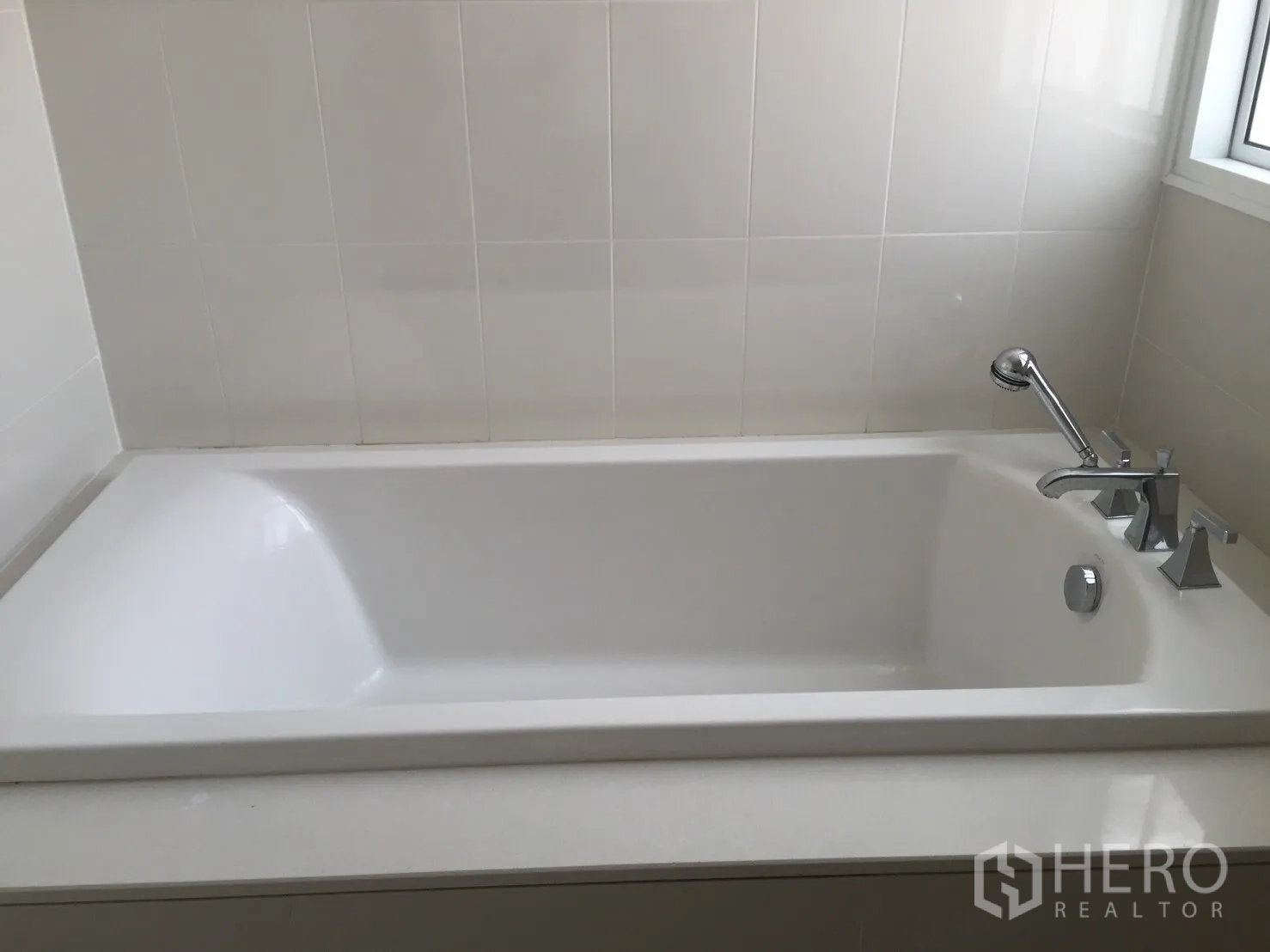 Townhouse for rent in Watthana, Bangkok - Clean bathroom featuring a white built-in bathtub with handheld shower by the window.