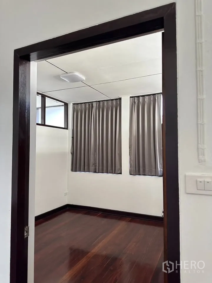Detached House for rent in Phra Khanong, Bangkok - Compact room with dark wood floor and grey curtains.
