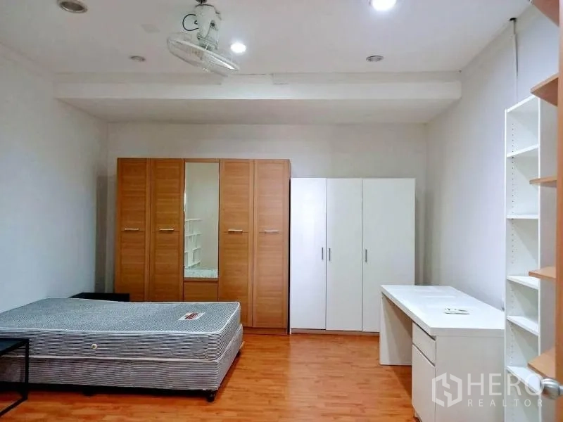 Condominium for rent in Khlong Toei, Bangkok - Large bedroom with multiple wardrobes, desk and ceiling fan on wood floors.