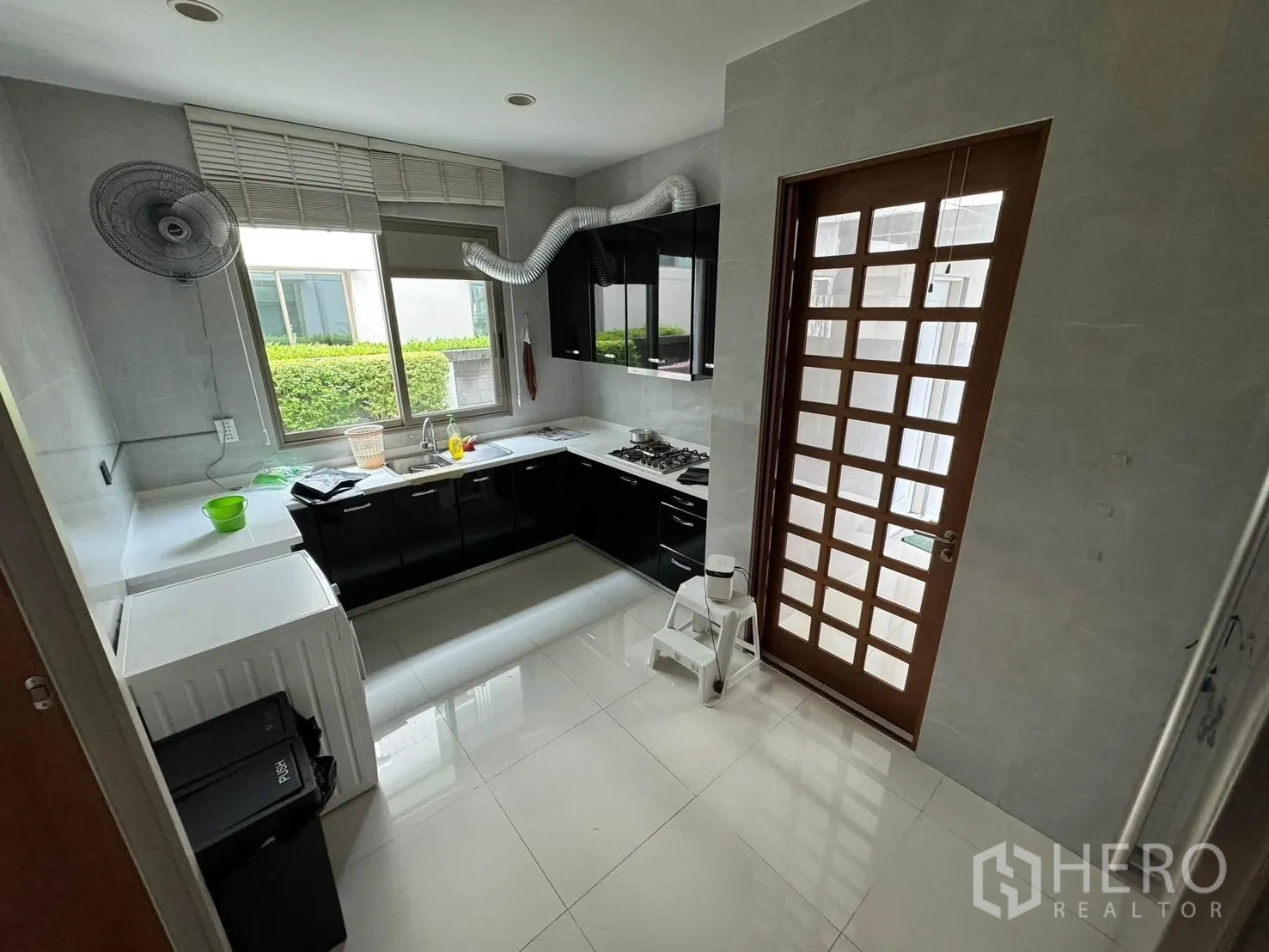 Detached House for rent in Prawet, Bangkok - Separate kitchen with black cabinetry, gas hob, window and side door.
