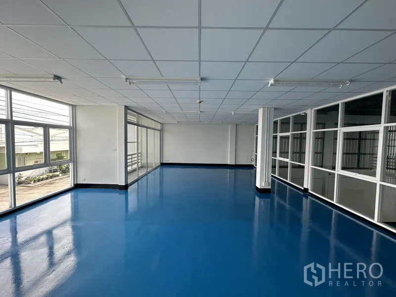 Factory for rent in Khlong Luang, Pathum Thani - Corner office with large windows and louvered sun‑screen, blue epoxy floor.