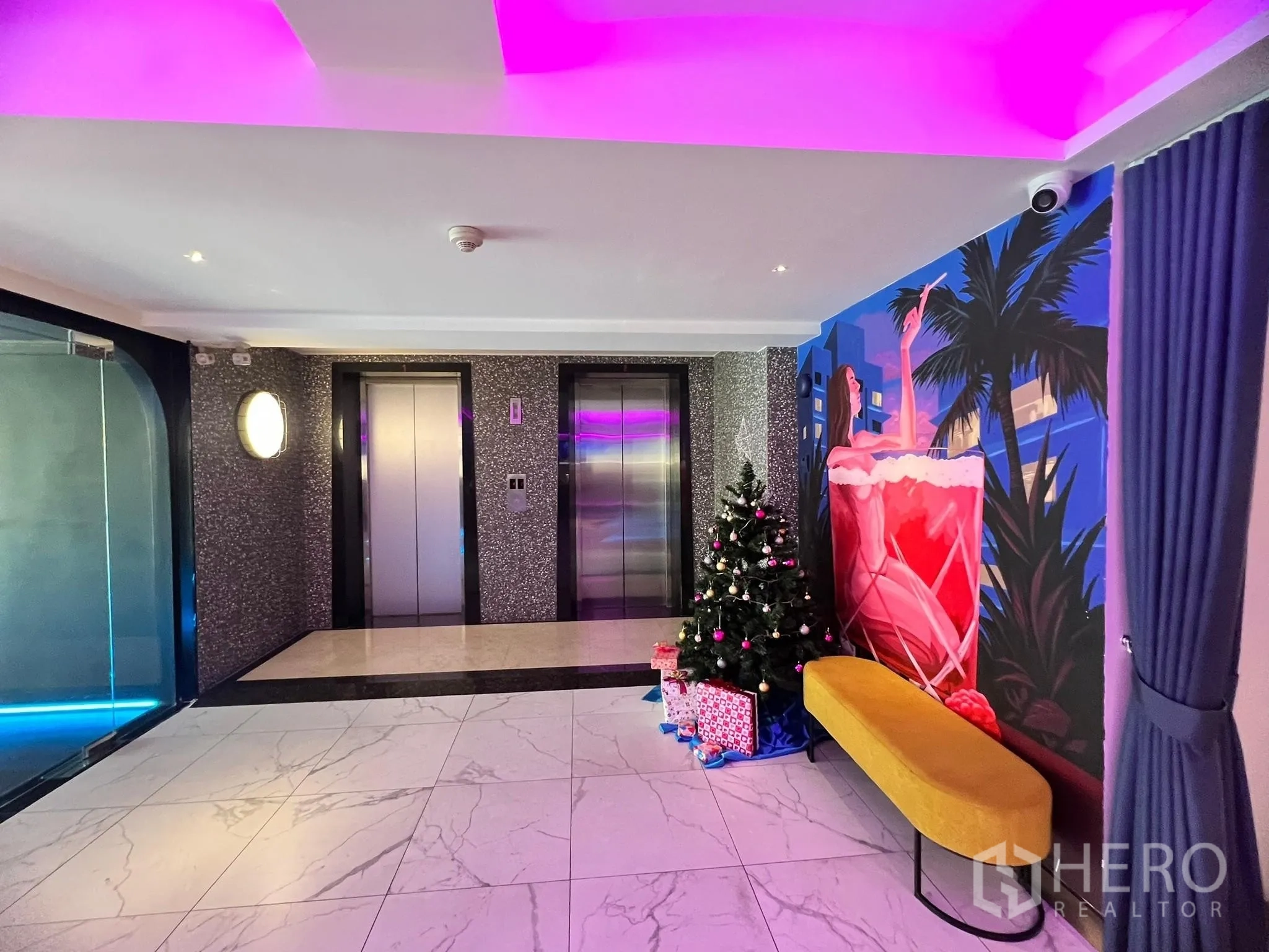 Retail Space for rent - Elevator lobby with two lifts, marble flooring, colorful mural and a bench in a commercial building.