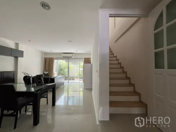 Townhouse for rent in Suan Luang, Bangkok - Bright open-plan living and dining area with stairs and sliding glass doors to a small patio.