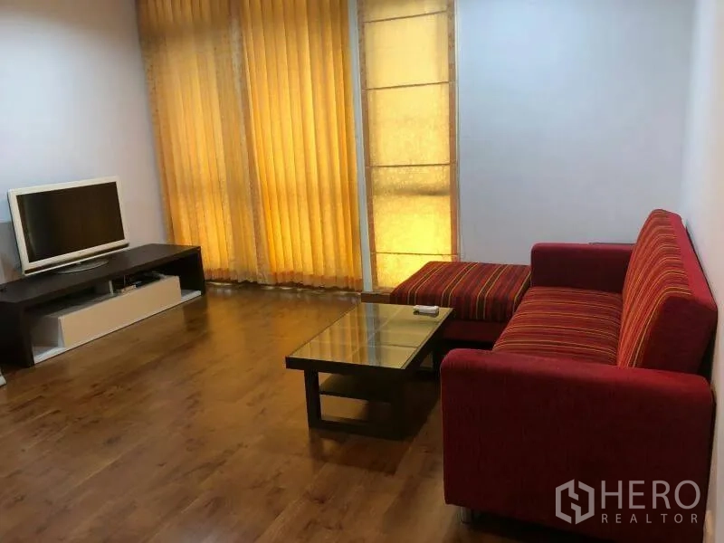 公寓 出租在Watthana, Bangkok - 明亮客厅，红色沙发、电视柜、玻璃茶几、木地板与暖色落地窗帘。