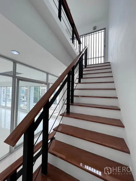 Home Office for sale in Lat Krabang, Bangkok - Staircase with wooden steps and metal handrail beside floor-to-ceiling windows.