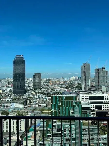 Condominium for rent - High-floor balcony view of Bangkok skyline with modern towers against a clear blue sky.