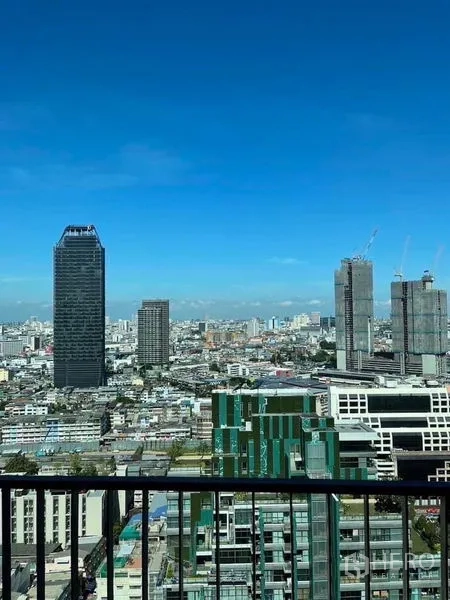 Condominium for rent - High-floor balcony view of Bangkok skyline with modern towers against a clear blue sky.
