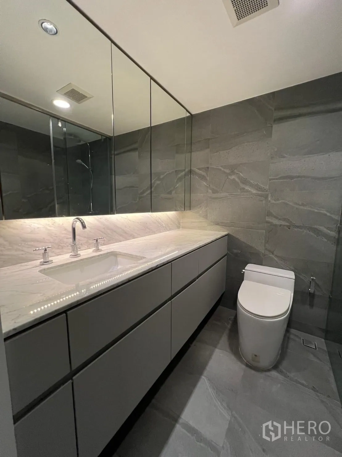 Condominium for rent or sale in Sathon, Bangkok - Guest bathroom with marble vanity, mirrored cabinets and gray stone tiles.