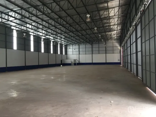 Warehouse for rent in Pathum Thani - Open warehouse hall with rows of high‑bay lights, skylight panels and smooth concrete flooring.