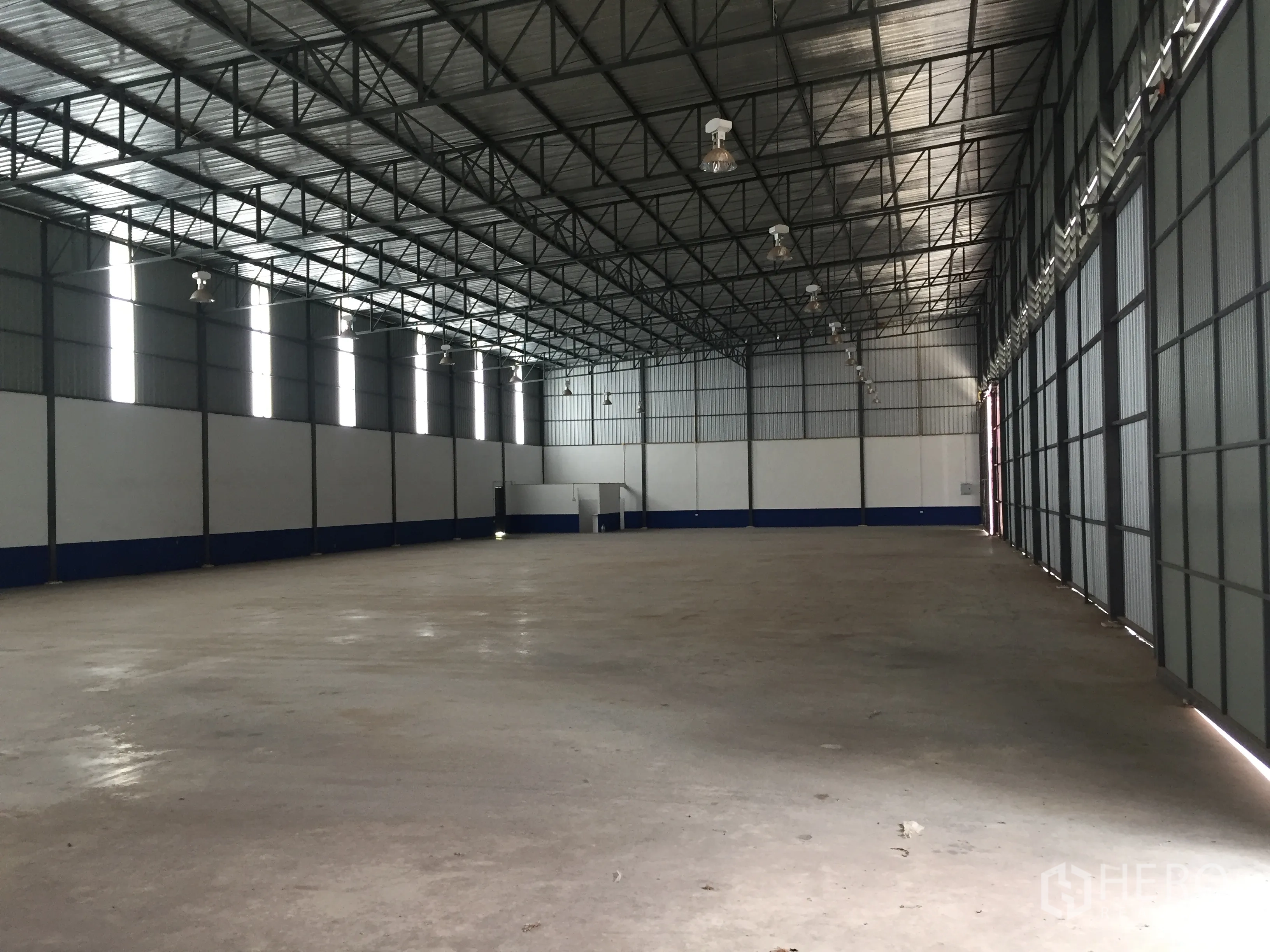 Warehouse for rent in Pathum Thani - Open warehouse hall with rows of high‑bay lights, skylight panels and smooth concrete flooring.