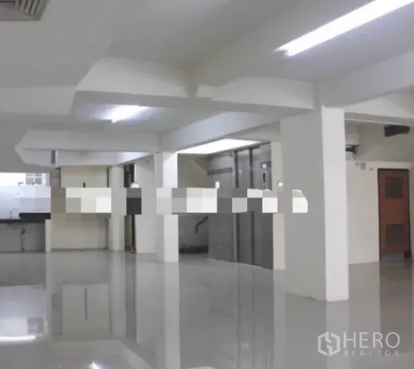 Shophouse for rent in Khlong Toei, Bangkok - Bright open-plan ground floor with polished tile flooring, structural columns, and an elevator lobby.