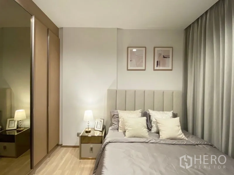 Condominium for rent or sale in Watthana, Bangkok - Cozy master bedroom with upholstered headboard, bedside lamps, mirrored wardrobe and soft gray bedding.