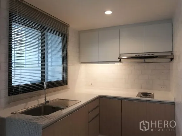 Townhouse for rent in Bang Kapi, Bangkok - Bright U-shaped kitchen with window blinds, white cabinets, stainless sink, cooktop and hood.